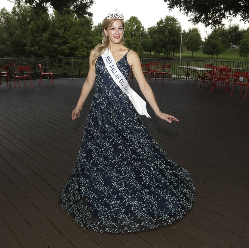 Amy Bosway wearing a crown and posing in a floor-length black and white dress and white sash with "Miss Dallas Co" on the front