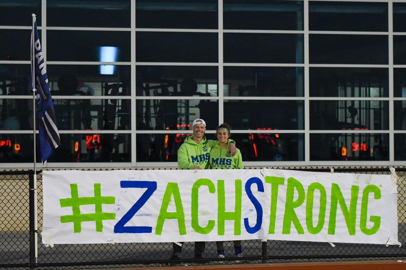Zach and his sister photographed while holding a white banner with the words "#ZachStrong" in blue and green paint