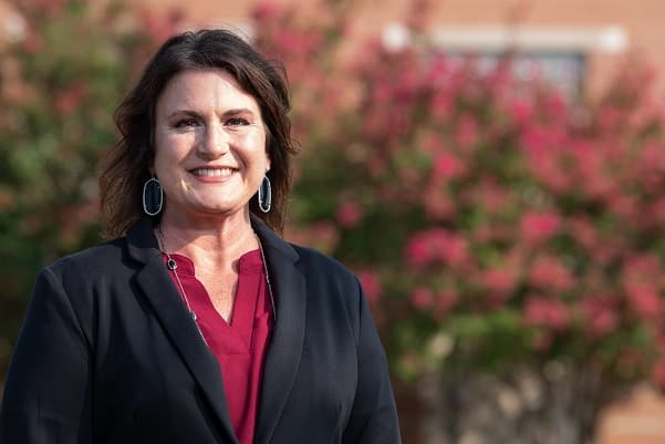 Midlothian ISD principal Hollye Walker photographed in a red blouse and black blazer in front of a rose bush and a brick building