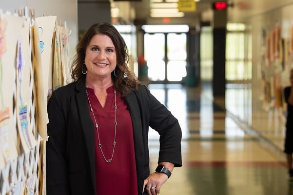 Midlothian ISD principal Hollye Walker photographed in a red blouse and black blazer in front of a school hallway