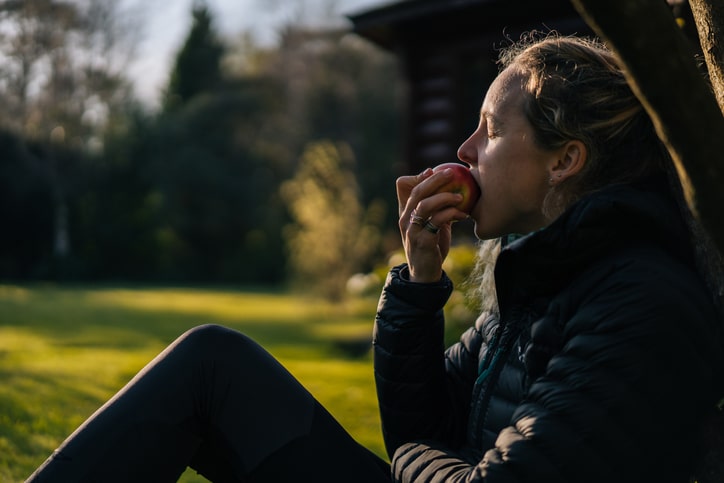 A woman photographed from her side, while she takes a bite out of an apple with her eyes closed