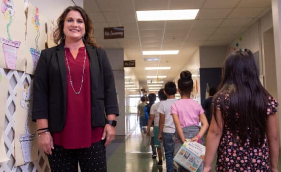 Midlothian ISD principal Hollye Walker photographed in a red blouse and black blazer in front of a hallway of schoolchildren