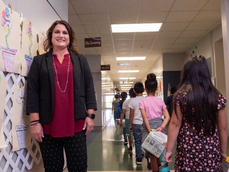Midlothian ISD principal Hollye Walker photographed in a red blouse and black blazer in front of a hallway of schoolchildren