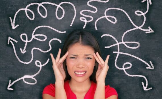 A stock image of a woman wearing a red cap sleeve blouse placing her fingers by the sides of her head, with a grimaced face, with squiggly lines spanning out around her, used to explain mindfulness