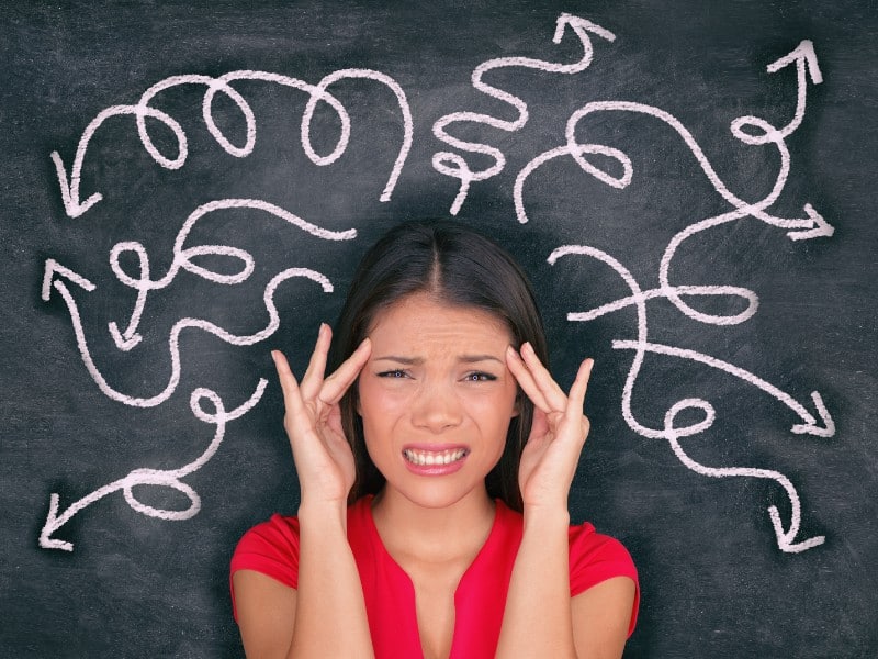 A stock image of a woman wearing a red cap sleeve blouse placing her fingers by the sides of her head, with a grimaced face, with squiggly lines spanning out around her, used to explain mindfulness
