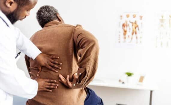 A medical profesional placing their hands on someone's back who is sitting in a medical appointment room, used to explain back pain and herniated disk