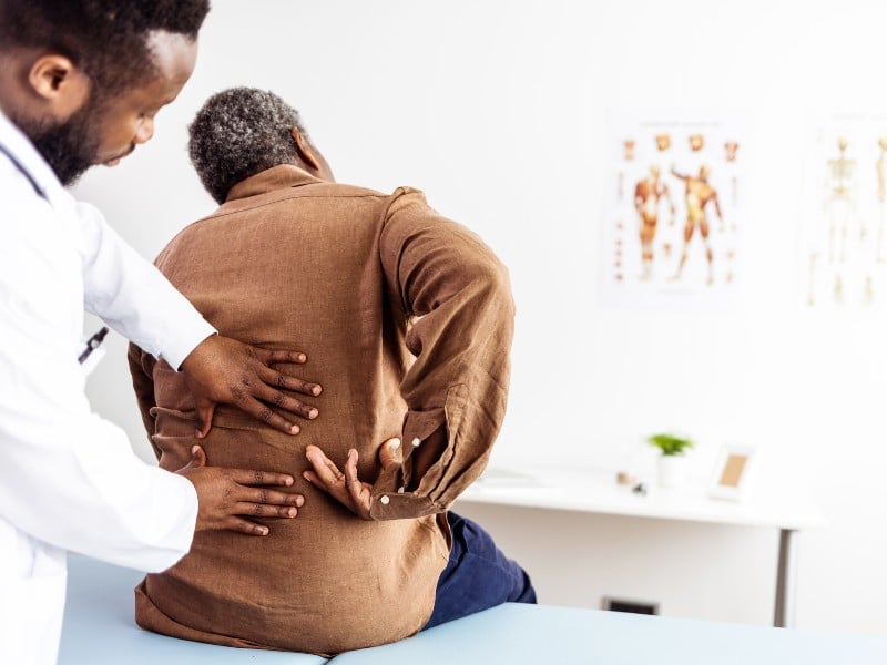 A medical profesional placing their hands on someone's back who is sitting in a medical appointment room, used to explain back pain and herniated disk