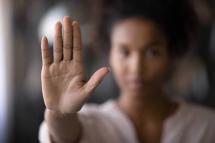 A woman holding up her hand with her palm toward the camera in focus and everything in the background blurry