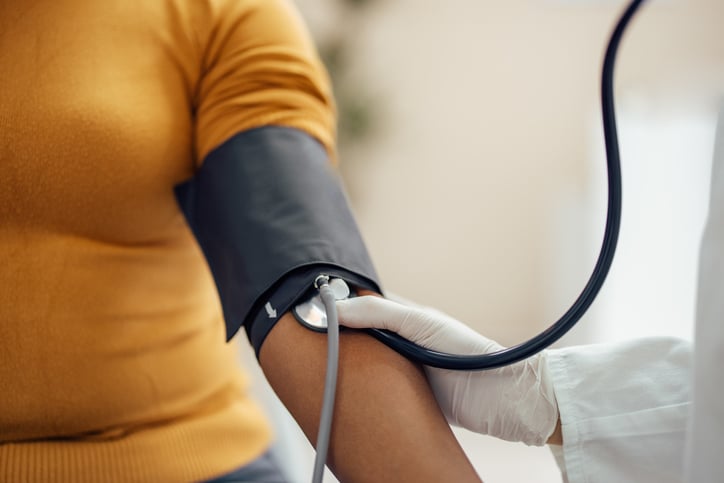 A medical professional taking a blood pressure reading from a women in an orange shirt