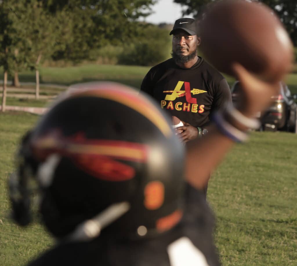 Rodney Seastrunk holding a football with a player throwing a ball in the foreground