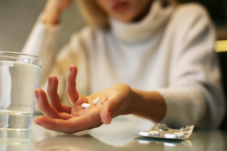 Woman holding two white pills in her hand with the glass of water and pill container in the foreground.