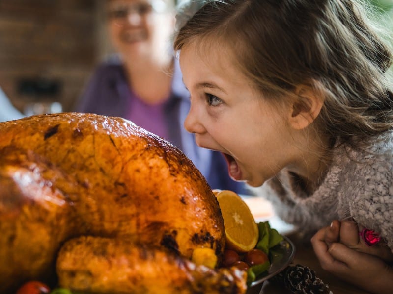 A child making a funny face toward a Thanksgiving turkey on a table