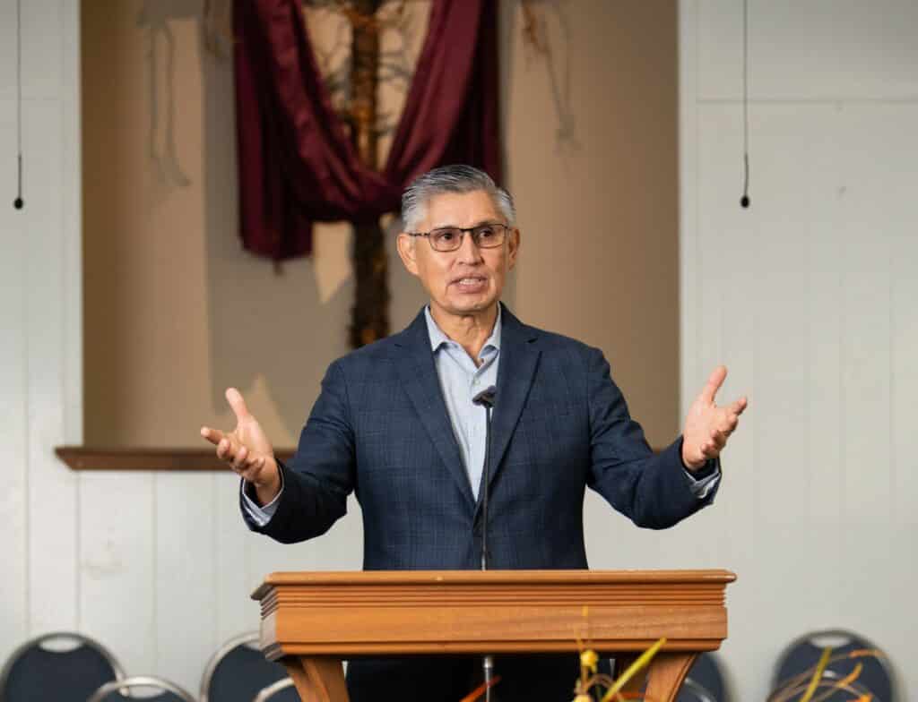 Pastor Arturo Malacara standing at a church puplit, used to explain his widow maker heart attack recovery