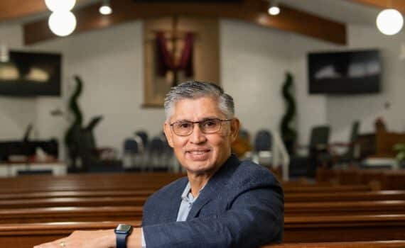 Pastor Arturo Malacara sitting in a church pew looking at the camera, used to explain his widow maker heart attack recovery