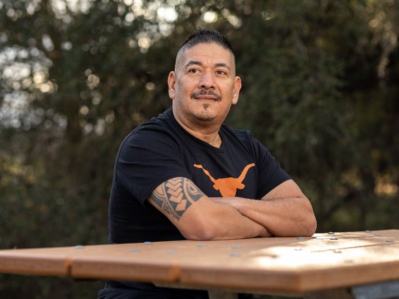 COVID-19 survivor Ray Hernandez photographed with a University of Texas t-shirt and his arms crossed, after becoming a COVID-19 survivor