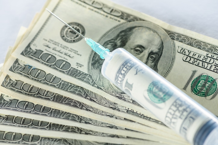 A needle with a hundred dollar bill inside of the syringe, with other hundred dollar bills in the background