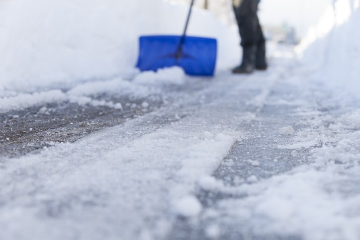 A blue snow shovel is pushed through an icy road.