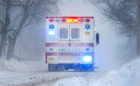 An ambulance drives down a city street during a snow storm, used to explain heart attacks and cold weather