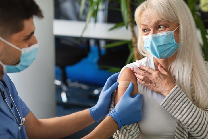 Woman looking at a medical professional with kind eyes as he places a bandaid on her upper arm