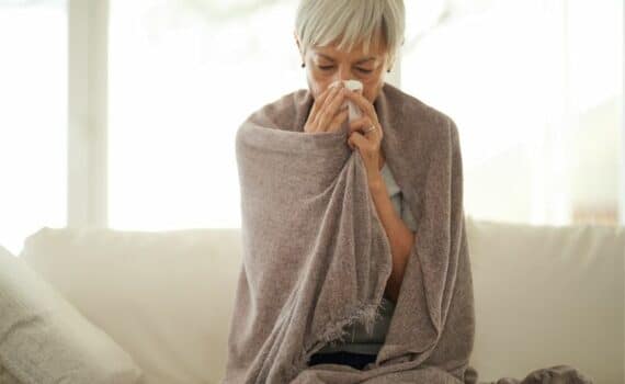 A woman wrapped in a blanket and holding a tissue to her nose and mouth, used to explain seniors and a potential RSV vaccine