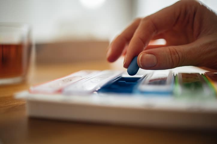 A close-up picture of a hand removing a blue antihistamine pill from a pill case