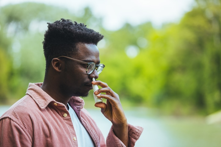 A young man in an outdoor setting uses an antihistamine nasal spray.