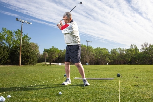 Security contractor Tom Eastman photographed in a collared golf shirt with trees in the background while golfing after hip and knee surgeries