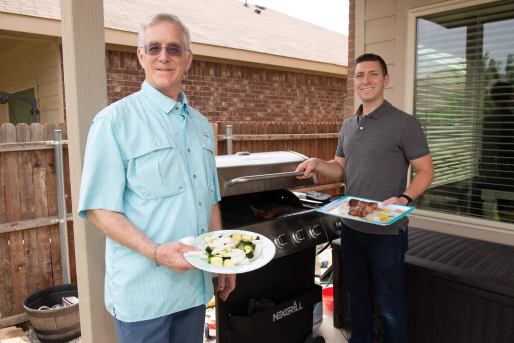 Doug and Collin Kidd standing next to a grill and smiling at the camera