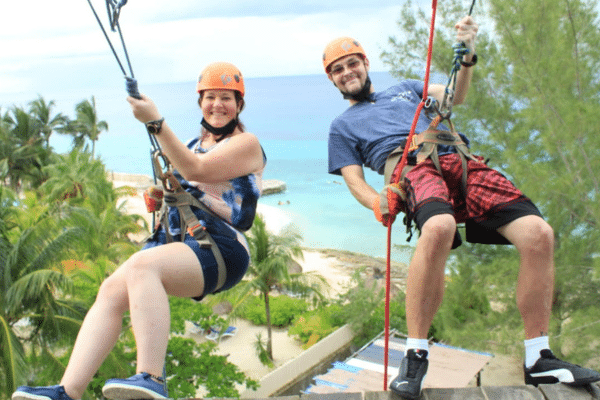 A man and a woman in helmets sit in seat harnesses as if about to go rock climbing.