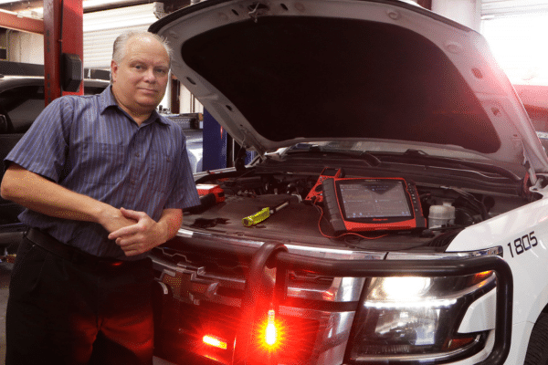 Roger Huseman, mechanic for the Ellis County police department, photographed standing in front of an open hood of an SUV