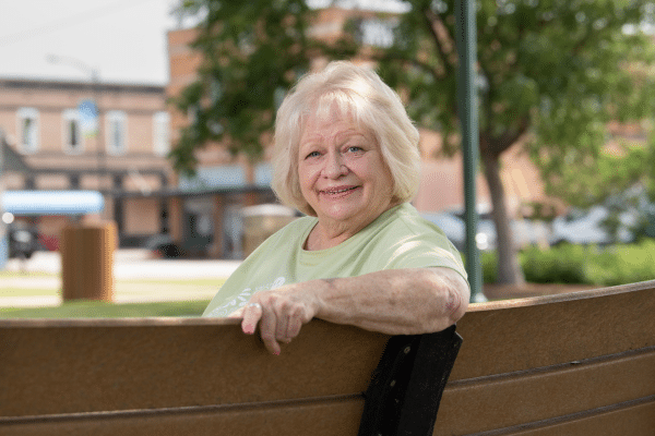 Joan Daniels, photographed smiling and sitting on a bench after her lung cancer treatment