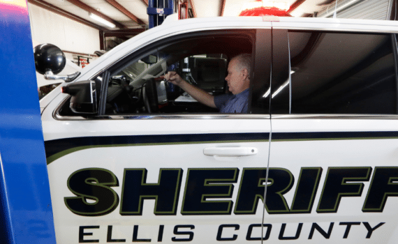 Roger Huseman, mechanic for the Ellis County police department, photographed sitting in the driver's seat of an officer's vehicle after his hernia repair