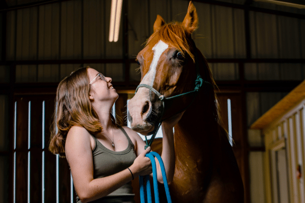 Photograph of Kathryn Altman as a young adult looking up at a horse and smiling