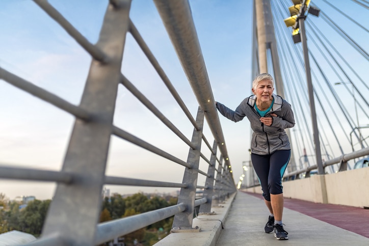 An older woman in exercise clothing holding a side rail along a bridge