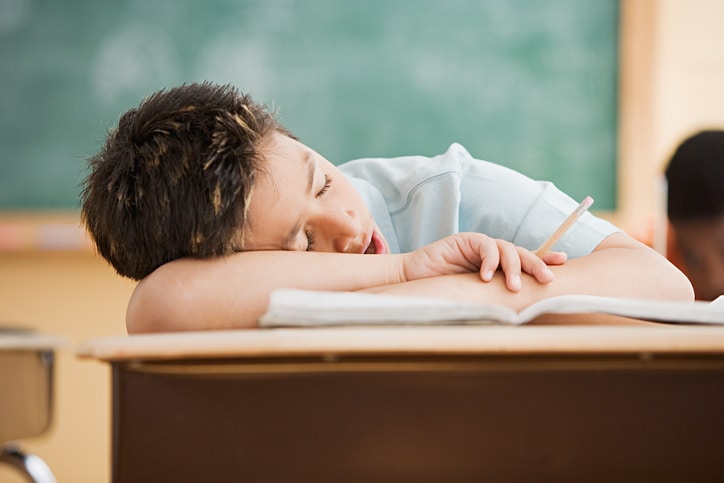 A young boy sleeping at his school desk with his mouth open