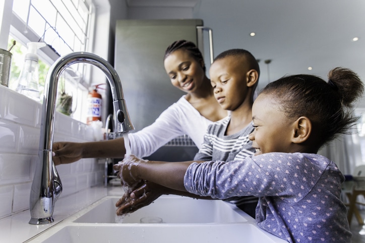 A caregiver helping two children wash their hands
