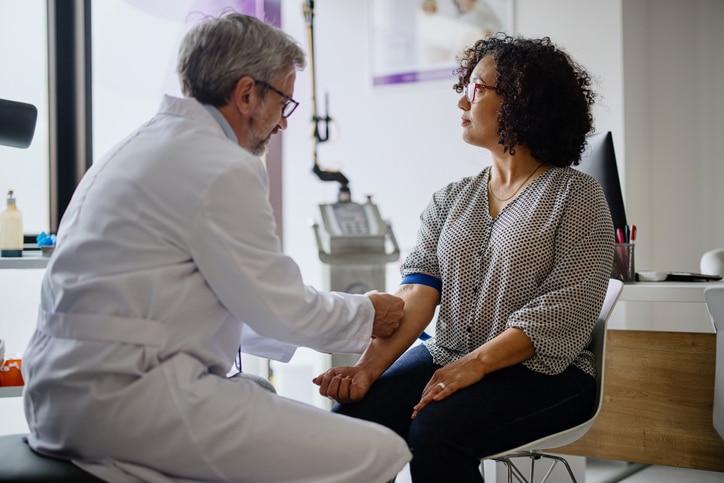 In an office setting, a doctor touches a woman's arm as she looks out a window.