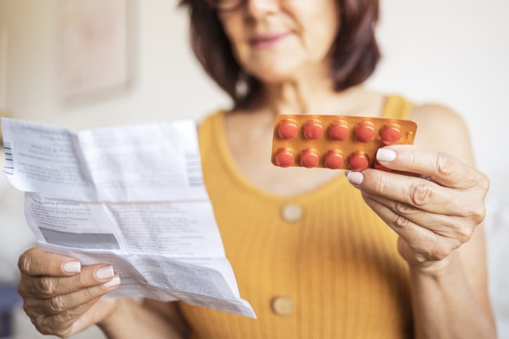 A woman holds a blister pack with pills and a piece of paper.