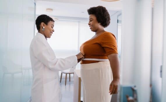 Woman standing next to medical provider who is measuring her abdomen, used to explain weight loss surgery benefits