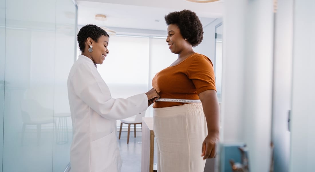 Woman standing next to medical provider who is measuring her abdomen, used to explain weight loss surgery benefits