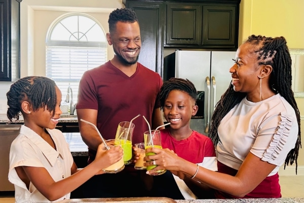A woman named Thandi Montgomery, her husband and their two children smiling and holding glasses with straws together, as if they were making a "cheers"
