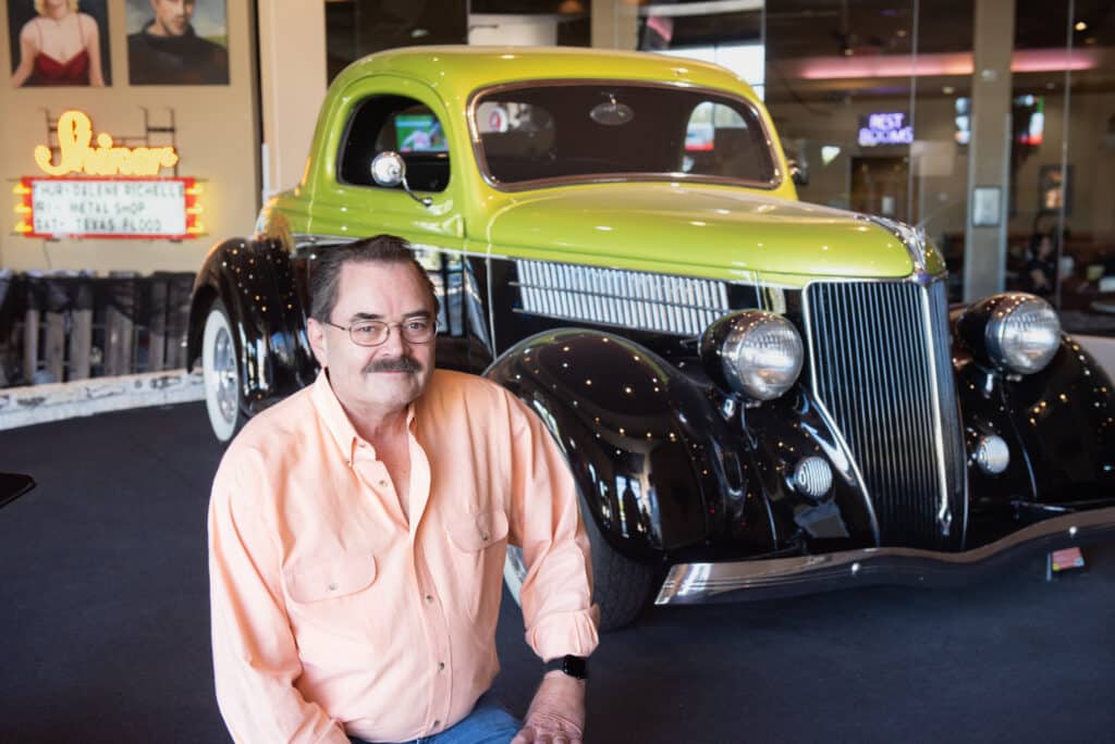 A man named Jack Crain sitting in front of a yellow and black classic car
