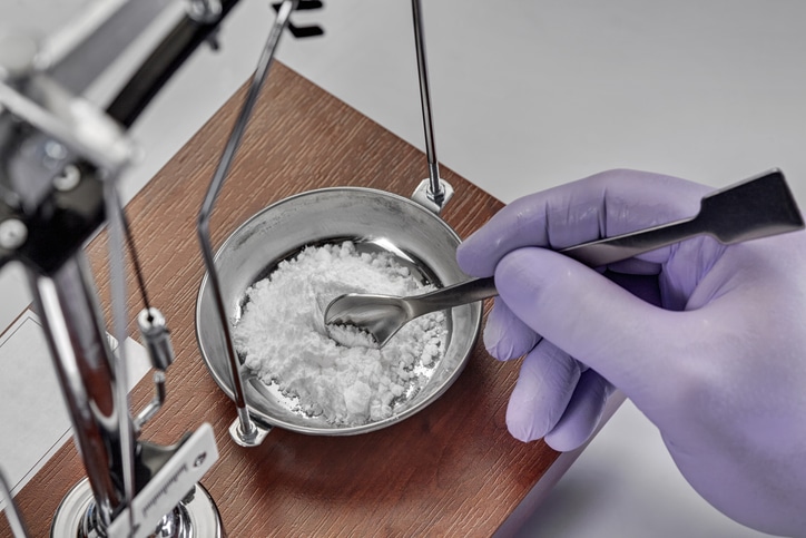 A pharmacist preparing medications by weighing a substance on a scale and stirring with a spoon-like tool