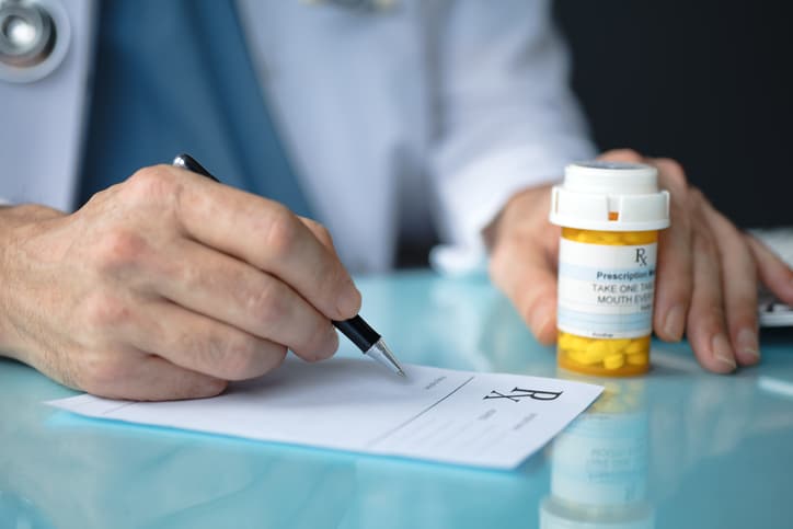 A medical professional in a white coat signing a prescription with a pill bottle in the foreground