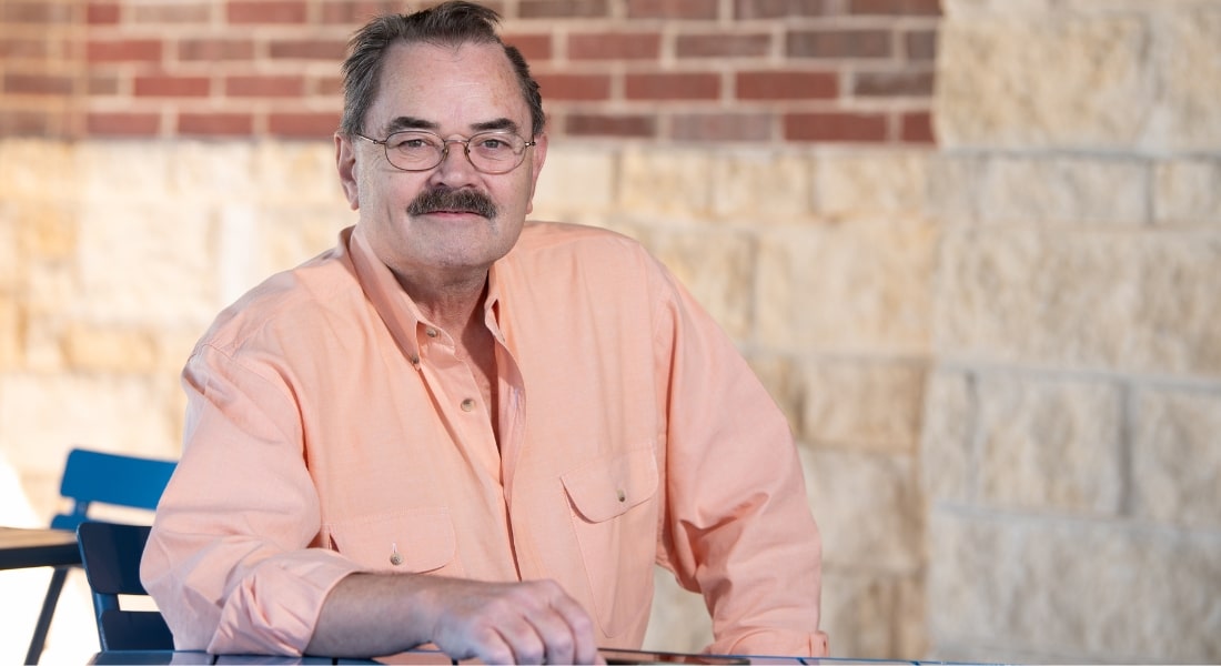 A man named Jack Crain photographed in an orange button down shirt while smiling and looking at the camera