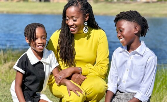 A woman named Thandi Montgomery wearing a bright yellow shirt and smiling and photographed with her two children with a lake in the background