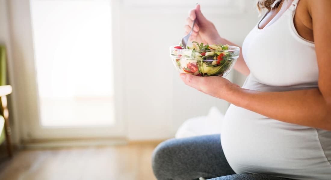 Stock image of a pregnant woman eating a salad, used to explain the best nutrients for mom and baby