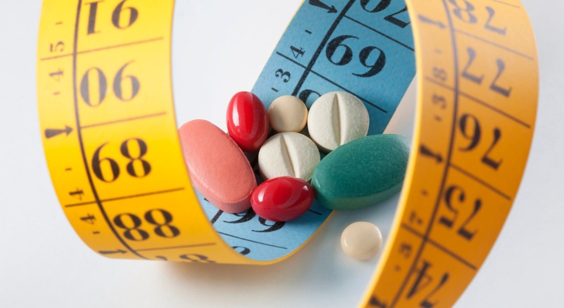 A stock image of a series of pills wrapped in a fashion tape measurer, used to explain weight-loss drugs