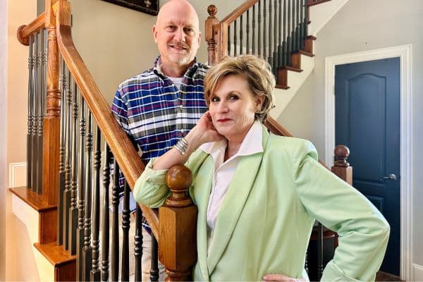 An older couple named Mark and Sandra Stewart photographed standing on a staircase and smiling at the camera