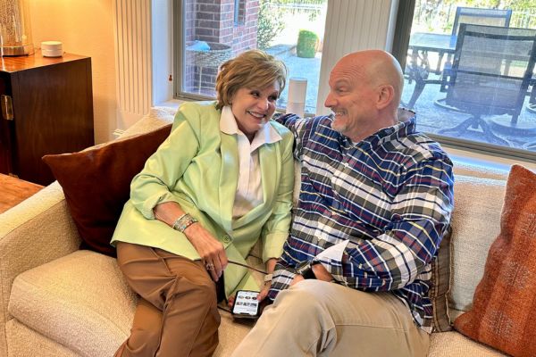 An older couple named Mark and Sandra Stewart photographed standing on a couch and smiling at each other